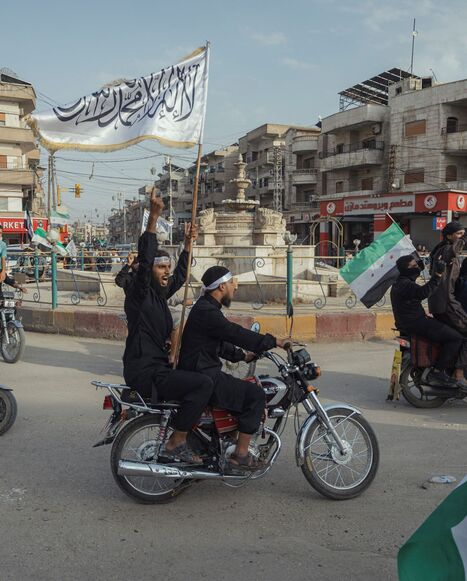 Demonstrators ride through a street while waving Syrian flags