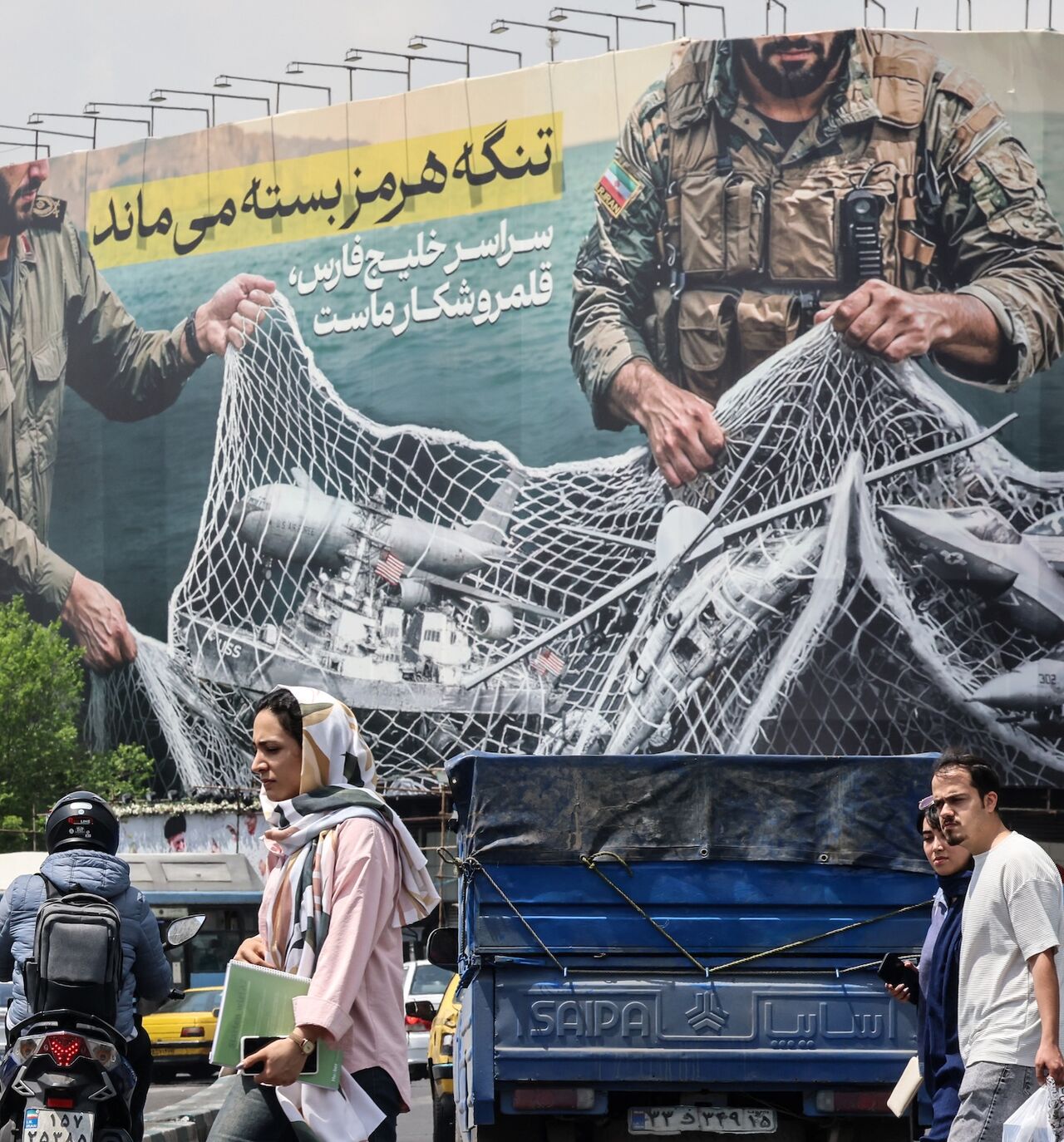 Iranian walks past a giant billboard reading "The Strait of Hormuz remains closed" at the Revolution Square in Tehran on April 22, 2026.