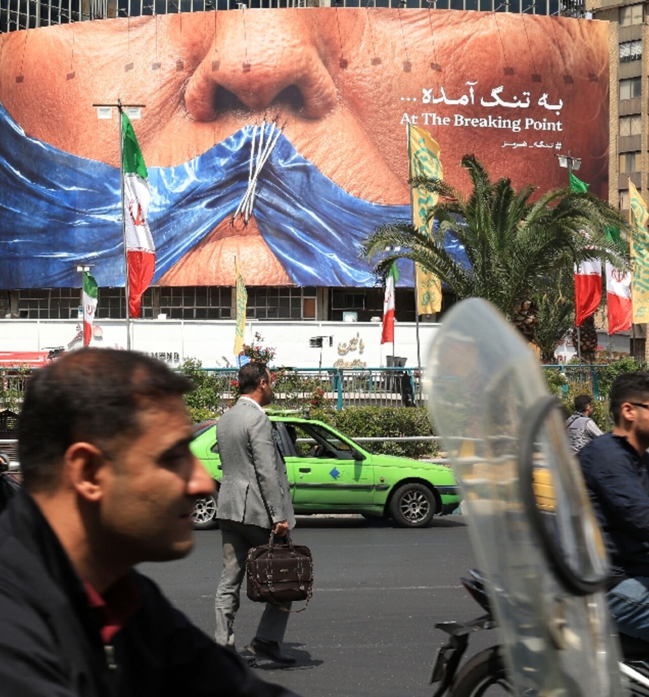 Commuters make their way past an anti-US billboard referring to President Donald Trump and the Strait of Hormuz, installed on a building at the Valiasr Square in Tehran