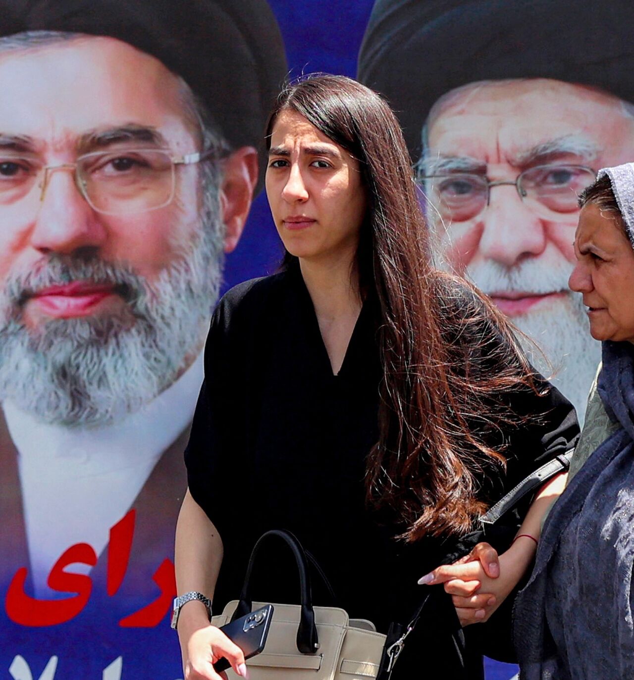 Women walk past a large banner depicting Iran's current supreme leader, Mojtaba Khamenei, and his predecessor and late father, Ali Khamenei, along a street in Tehran on May 6, 2026.