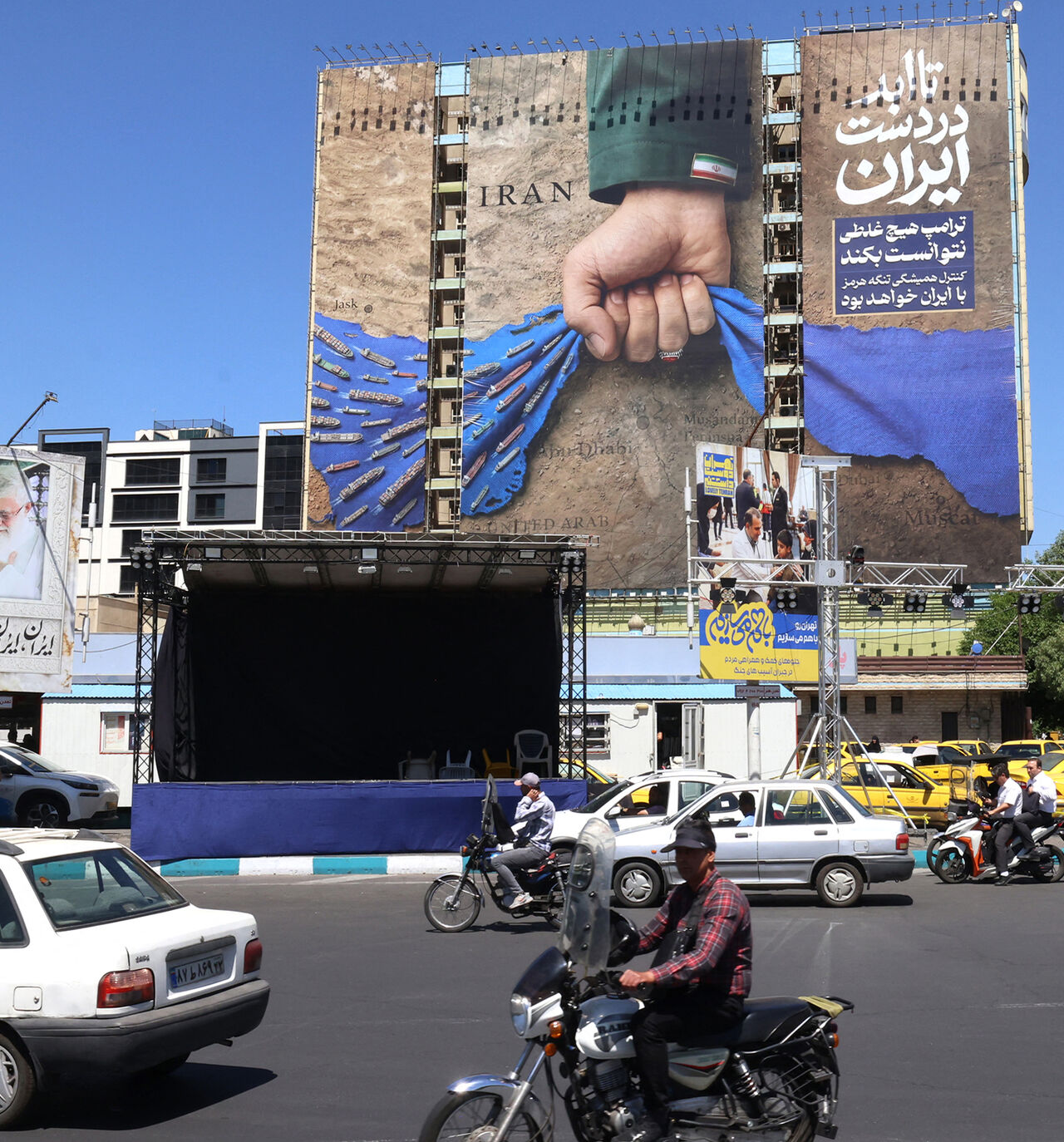Vehicles drive past a billboard on the facade of a building depicting the Strait of Hormuz with a caption in Persian reading, "Forever in Iran's Hand," at Vanak Square, Tehran, Iran, May 25, 2026.