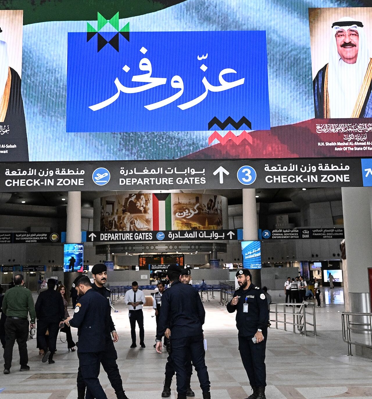 Kuwaiti security officers stand beneath a screen displaying portraits of the Emir of Kuwait Sheikh Meshal al-Ahmad al-Jaber al-Sabah (R) and the Kuwaiti crown prince Sheikh Sabah al-Khaled al-Hamad al-Sabah, alongside the words "Pride and Glory", at Kuwait International Airport in Kuwait City on June 1, 2026, as the airport resumes operations following a phased reopening plan. 