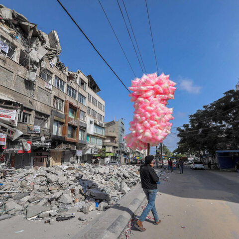 A Palestinian pedlar walks with bags of cotton candy past the rubble of a building destroyed during the May 2021 conflict between Hamas and Israel in al-Rimal neighborhood, Gaza City, Gaza Strip, June 10, 2021.