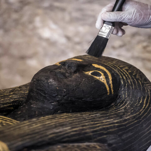 An Egyptian archaeologist brushes the top of a carved black wooden sarcophagus inlaid with gilded sheets, dating to Egypt's Late Period (7th-4th century BC), on the west bank of the Nile north of the southern city of Luxor, Egypt, Nov. 24, 2018.