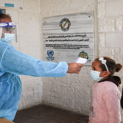 An employee of the United Nations Relief and Works Agency for Palestine Refugees measures the body temperature of a girl as people arrive to receive the Sputnik V COVID-19 vaccine at UNRWA's clinic in Rafah camp, southern Gaza Strip, March 3, 2021.