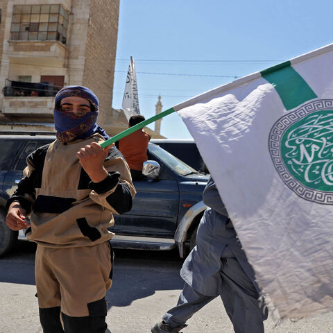 A member of Hayat Tahrir al-Sham holds the group's flag as others parade with their flags and those of the Taliban's declared "Islamic Emirate of Afghanistan" through the rebel-held city of Idlib, Syria, Aug. 20, 2021.