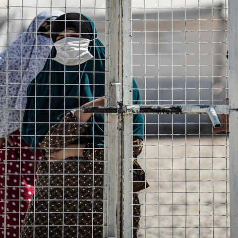 A woman stands by a metal fence at Roj camp that houses family members of people accused to belong to the Islamic State and who were relocated from al-Hol camp, in the countryside near al-Malikiyah, Hasakah province, Syria, Sept. 30, 2020.