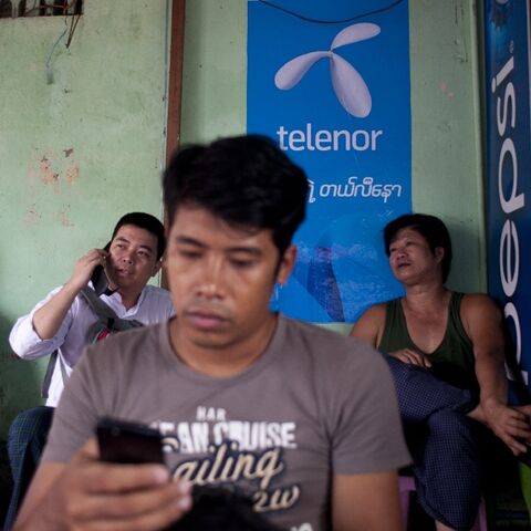A man uses a phone in front of a Telenor advertising board in Yangon