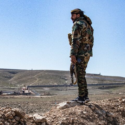 A member of the border guard force loyal to the Syrian Democratic Forces (SDF) looks on near Syria's town of al-Hol at ongoing construction of a concrete border fence being erected on the Iraqi side