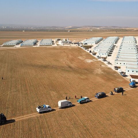 Internally displaced Syrians arriving with their belongings in a convoy of trucks, at a new housing complex. 
