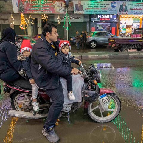 A man rides a scooter with a woman and two children along a main street adorned with Christmas and New Year's decorations, in the northern suburb of Shubra (home to a large Christian population), Cairo, Egypt, Dec. 31, 2021.