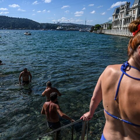 wimmers enter the water in the Bosphorus strait in Istanbul's Bebek district on July 29, 2022. - Istanbul, a historic megalopolis of 16 million people resting between two continents and two sea, does not bring to mind immediate images of a beach resort. But just like the locals of New York, Beirut and a handful of other global cities, Istanbulites can swim all summer long and return home on the metro with salt layering their skin, sand trapped under their sandals. (Photo by Ozan KOSE / AFP) (Photo by OZAN K