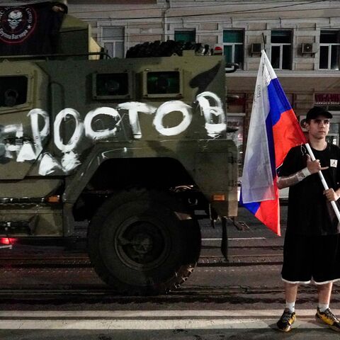A man holds the Russian national flag in front of a Wagner group military vehicle with the sign read as "Rostov" in Rostov-on-Don late on June 24, 2023. Rebel mercenary leader Yevgeny Prigozhin who sent his fighters to topple the military leaders in Moscow will leave for Belarus and a criminal case against him will be dropped as part of a deal to avoid "bloodshed," the Kremlin said on June 24. (Photo by STRINGER / AFP) (Photo by STRINGER/AFP via Getty Images)