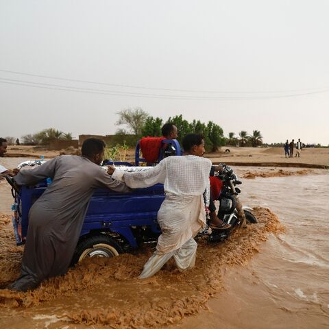 People push a vehicle through muddy flood water following torrential rains in Saqqai near Sudan's capital Khartoum