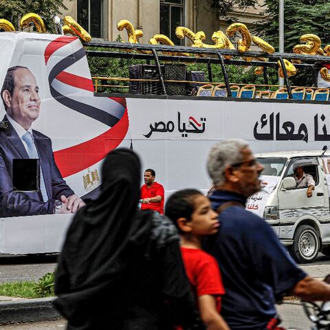 A man, child, and woman ride a motorcycle across the street from an election campaign bus for Egypt's President Abdel Fattah al-Sisi adorned with his image and slogan "Long Live Egypt"