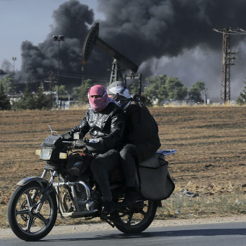 People ride on a motorcycle as thick smoke rises from an oil extracting facility targeted by Turkish shelling near Syria's northeastern border with Turkey in the Qahtaniyah countryside in the far northeast corner of Hasakeh province on Oct. 25, 2024.