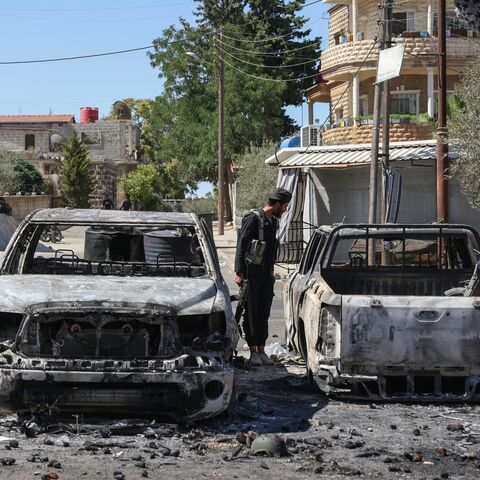 A member of the Syrian security forces examines burnt vehicles amid ongoing clashes in the southern Syrian city of Suwayda, July 16, 2025. 
