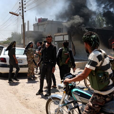 Fighters from Bedouin tribes gather near a burning building in al-Mazraa village, in Syria's southern Suwayda governorate, as clashes with Druze gunmen continue, on July 18, 2025. 