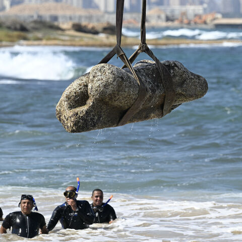 Divers watch as a crane pulls an artifact from the waters at Abu Qir bay in Alexandria on Aug. 21, 2025, as part of an event organized by the Ministry of Tourism and Antiquities to recover sunken antiquities. 