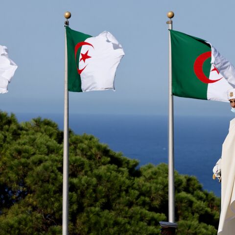 A man wearing a traditional cloth walks past national flags of Algeria near the Bay of Algiers in Algiers, on Aug. 25, 2022.