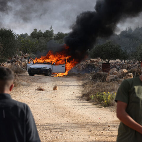 TOPSHOT - Palestinians stand near a burning car reportedly set alight by Israeli settlers attempting to disrupt them harvesting olives near the occupied West Bank village of Turmos Ayya near Ramallah on October 19, 2025. (Photo by HAZEM BADER / AFP) (Photo by HAZEM BADER/AFP via Getty Images)