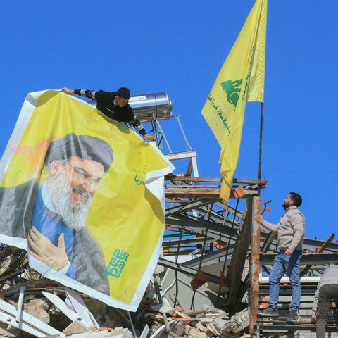 Residents hang a poster bearing a portrait of Hezbollah's slain leader Hassan Nasrallah and the flag of the Iran-baked party on the rubble of a destroyed house in the southern border village of Adaisseh, following the Israeli army's withdrawal on Feb. 18, 2025. 