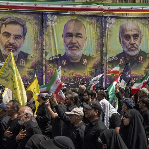People hold flags near posters displaying assassinated IRGC military leaders during a state funeral service in Enqelab Square on June 28, 2025, in Tehran, Iran.