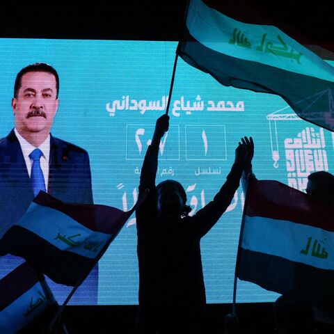 Supporters of incumbent Iraqi Prime Minister Mohammed Shia al-Sudani wave national flags in front of a screen displaying his portrait as they celebrate following the announcement of preliminary election results in Baghdad on Nov. 12, 2025.