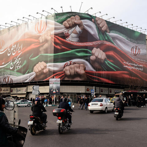 Vehicles pass by a large patriotic banner depicting the Iranian flag on Enghelab Square in Tehran on January 14, 2026. 