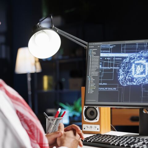 Detailed image of Middle Eastern developer in front of desktop pc monitoring a complex network, ensuring data security and efficient computing using cloud, AI and machine learning.