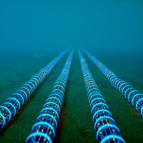 High-tech fiber optic cables glowing with blue light extend into the distance on the ocean floor — Getty Images Stock Photo