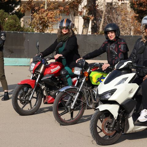 Iranian instructor Maryam Ghelich stands with student Narghes as they look at Elham (3rd R), Leila and Mona, posing on their motorbikes before their lesson at a training center in northern Tehran on Dec. 7, 2025.