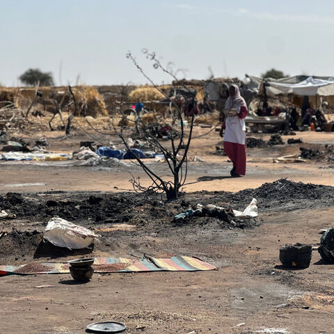 A displaced Sudanese woman who left El-Fasher after its fall with others, walks amid the remains of a fire that broke out at a camp in Tawila on Feb. 11, 2026. 