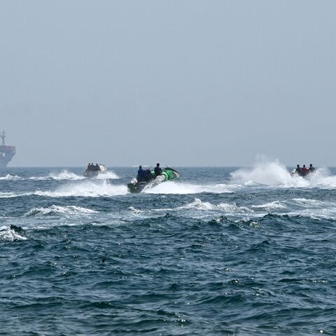 Small boats loaded with merchandise sail past the St. Kitt's and Nevis-flagged container ship Marsa Victory in the waters of the Strait of Hormuz off the coast of Khasab in Oman's northern Musandam Peninsula, on June 25, 2025.
