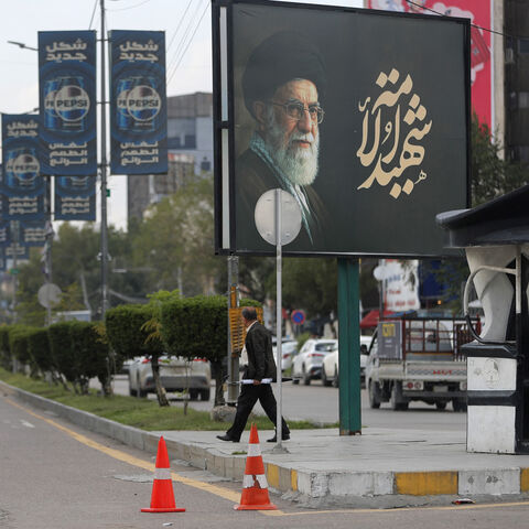 An Iraqi police officer stands guard as a man walks beneath a billboard bearing a portrait of Iran's slain supreme leader Ayatollah Ali Khamenei in Baghdad on March 25, 2026. Iraq will submit a formal complaint to the United Nations Security Council over strikes in its territory, the office of the prime minister said on March 25, following an attack in the country's west that killed seven security personnel. Iraq has been drawn into the Middle East war triggered by the US-Israel attack on its neighbour Iran