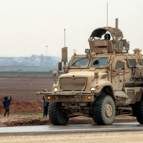Boys along a road wave to an approaching US military mine-resistant ambush protected (MRAP) armored fighting vehicle moving in a convoy transporting Islamic State group detainees being transferred to Iraq from Syria, on the outskirts of Qahtaniyah in Syria's northeastern Hasakah province on Feb. 7, 2026.