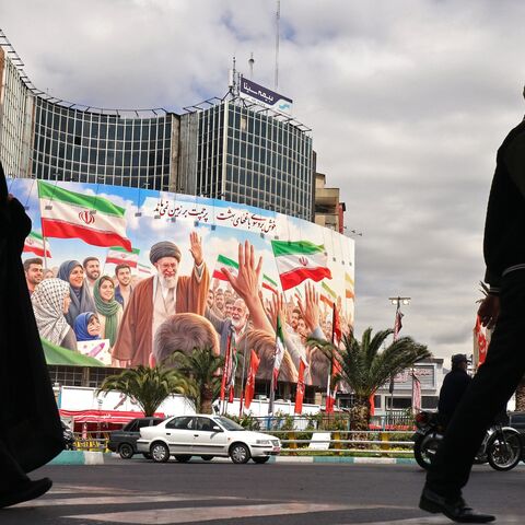 Commuters make their way past a giant billboard of slain Iranian supreme leader Ayatollah Ali Khamenei at Valiasr Square in Tehran on April 19, 2026. 