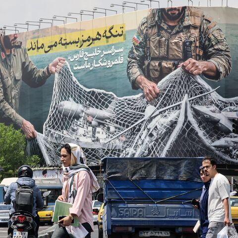 Iranian walks past a giant billboard reading "The Strait of Hormuz remains closed" at the Revolution Square in Tehran on April 22, 2026.