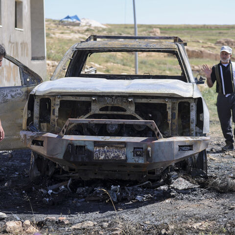 Two men stand next to the burned remains of a Palestinian vehicle in the Wadi al-Rakhim area of Susya village in Masafer Yatta, south of Hebron in the Israeli-occupied West Bank, on May 1, 2026. 