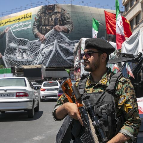An Iranian police office stands on patrol near a poster depicting Iranian soldiers holding a net in the shape of the Strait of Hormuz, with US military aircraft ensnared in a fishing net, on May 9, 2026 in Tehran, Iran. 