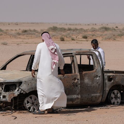 Men gather around the husk of a destroyed pickup truck that was driven by a local shepherd who was reportedly struck by Israeli forces and buried by locals at a grave nearby, in the Najaf desert in southwestern Iraq, on May 12, 2026. 