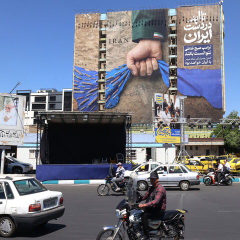 Vehicles drive past a billboard on the facade of a building depicting the Strait of Hormuz with a caption in Persian reading, "Forever in Iran's Hand," at Vanak Square, Tehran, Iran, May 25, 2026.