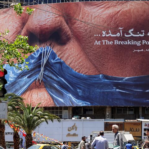 Motorists drive their vehicles and pedestrians cross the street past a political billboard featuring President Donald Trump and the Strait of Hormuz along Valiasr Square in Tehran on May 26, 2026.