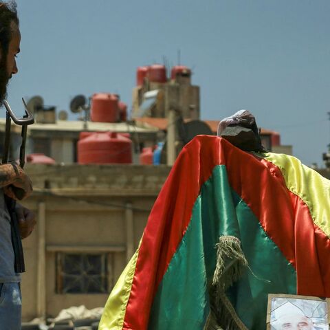 A Druze fighter stands at a roundabout draped with the Druze flag and a portrait of a local leader in the predominantly Druze city of Suwayda in southern Syria on July 21, 2025.