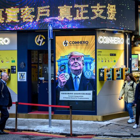 People walk past a cryptocurrency exchange office with a screen featuring US President Donald Trump holding cryptocurrency coins in Hong Kong on March 12, 2025.