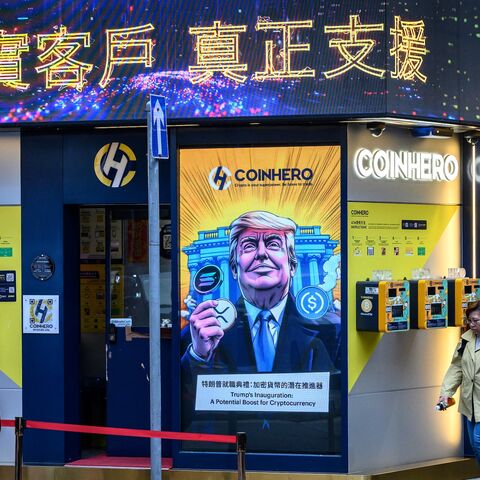 People walk past a cryptocurrency exchange office with a screen featuring US President Donald Trump holding cryptocurrency coins in Hong Kong on March 12, 2025.