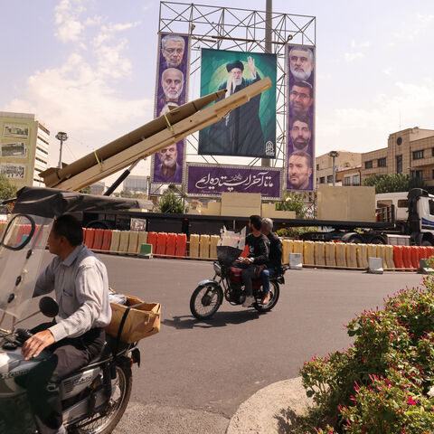 Iranians ride their motorcycles past a deactivated Kheibar Shekan ballistic missile in front of a picture of Iran's Supreme Leader Ayatollah Ali Khamenei in Tehran's Bahrestan Square on September 27, 2025, as part of an exhibit to mark the "Sacred Defense Week" commemorating the 1980-88 Iran-Iraq war. (Photo by ATTA KENARE / AFP) (Photo by ATTA KENARE/AFP via Getty Images)