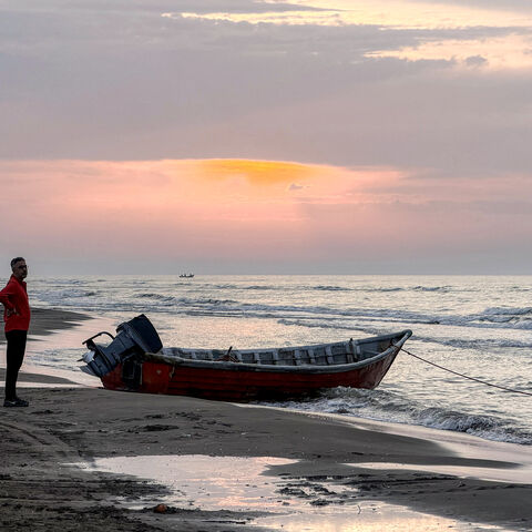 A man stands near a boat moored along a beach on the Caspian Sea coast in Sorkhrud in Iran's northern Mazandaran province on March 24, 2026, where many families have relocated due to the ongoing war with the US and Israel. Israel and the United States launched strikes on Iran on February 28, killing the Islamic republic's supreme leader and sparking a war that has since spread across the Middle East. (Photo by ATTA KENARE / AFP via Getty Images) /