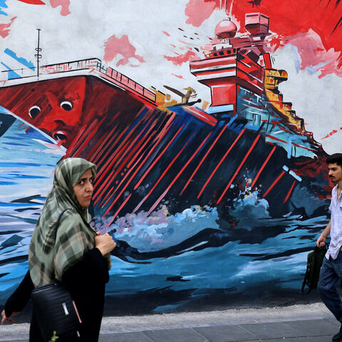 Commuters walk past a wall mural along the street in Tehran on July 21, 2026. Iran's Revolutionary Guards said on July 21 they hit US military targets including air defence systems in Bahrain and Kuwait, state news agency IRNA reported. (Photo by ATTA KENARE / AFP via Getty Images) /