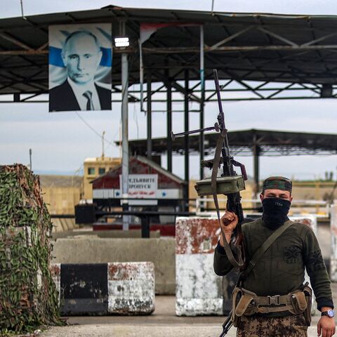 A Syrian rebel fighter looks on as he stands at an inspection checkpoint for incoming vehicles before a Russian flag and Russian soldiers behind manning the entrance of the Russian-leased Syrian military base of Hmeimim in Latakia province in western Syria on Dec. 29, 2024. 